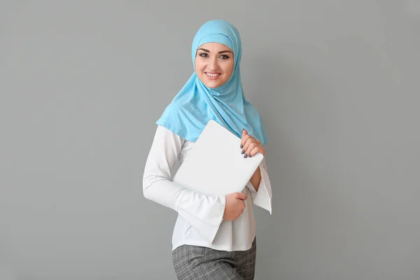 Schöne arabische Frau mit Laptop auf grauem Hintergrund — Stockfoto