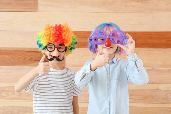 Little children in funny disguise showing thumb-up gesture on wooden background. April fools' day celebration — Stock Photo, Image