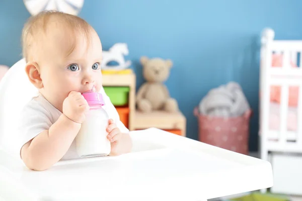 Baby with bottle of milk sitting in high-chair at home Stock Picture