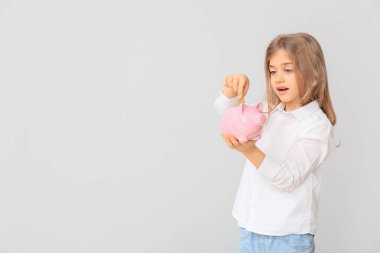 Tatlı kız, beyaz arka planda kumbaraya para yatırıyor.