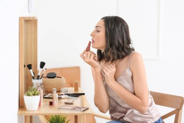 Güzel genç bir kadın evde makyaj yapıyor.