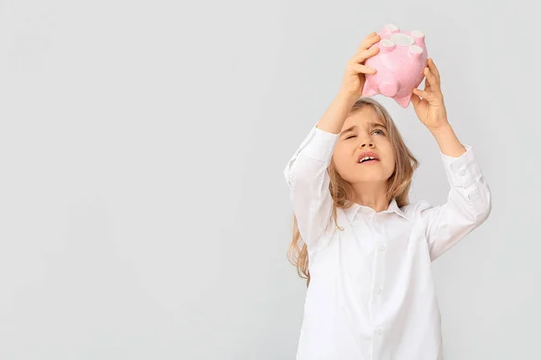 Cute girl tipping money from piggy bank on white background — Stock Photo, Image