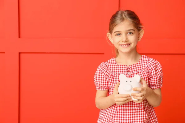 Cute girl with piggy bank on color background — Stock Photo, Image