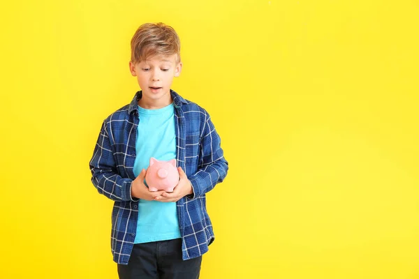 Cute boy with piggy bank on color background — Stock Photo, Image