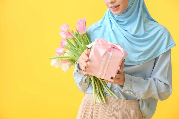 Gyönyörű muszlim nő virágokkal és ajándék a színes háttér. Nemzetközi nőnapi ünneplés — Stock Fotó