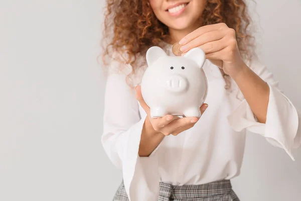 African-American woman with piggy bank on light background — Stock Photo, Image