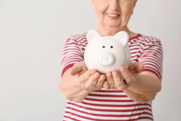 Mulher sênior feliz com banco porquinho no fundo leve — Fotografia de Stock