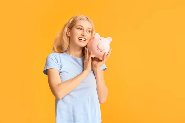 Jovem com banco porquinho no fundo de cor — Fotografia de Stock