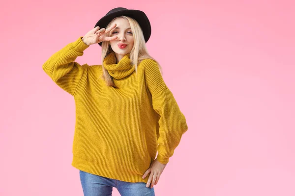 Young woman in warm sweater showing victory gesture on color background — Stock Photo, Image