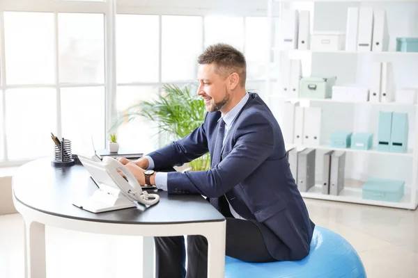 Businessman sitting on fitness ball while working in office