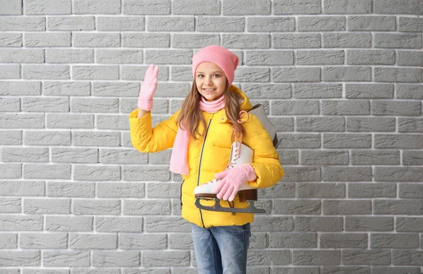 Cute little girl with ice skates on grey brick background — Stock Photo, Image