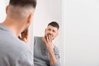 Memnuniyetsiz bir adam aynaya bakıyor.