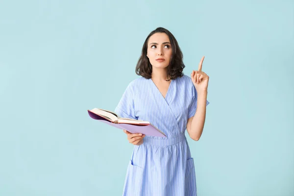 Beautiful young woman with book and raised index finger on color background