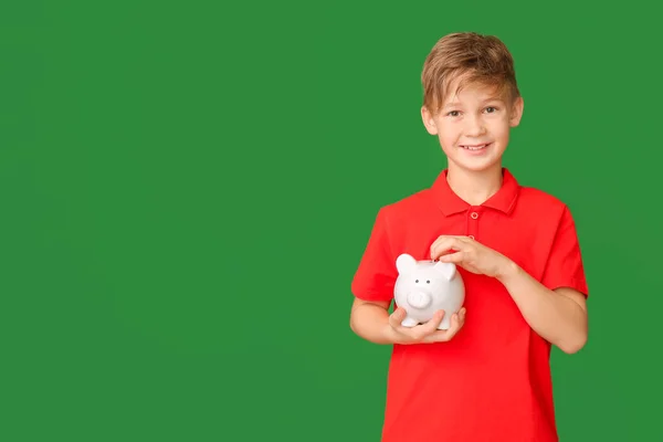 Cute Boy Putting Money Piggy Bank Color Background — Stock Photo, Image