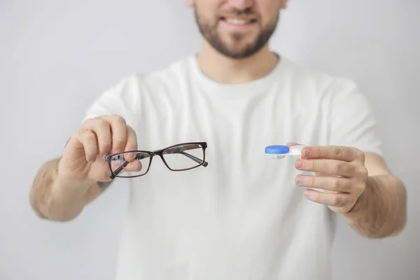 Handsome man with contact lens case and eyeglasses on grey background, closeup