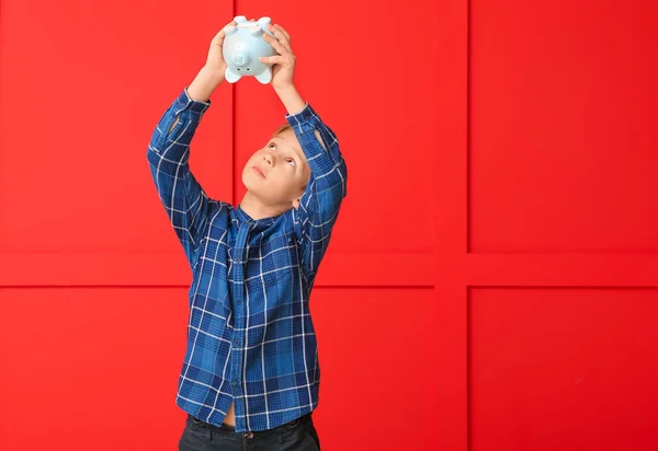 Cute boy tipping money from piggy bank on color background