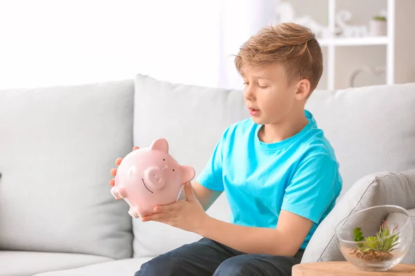 Cute boy with piggy bank at home