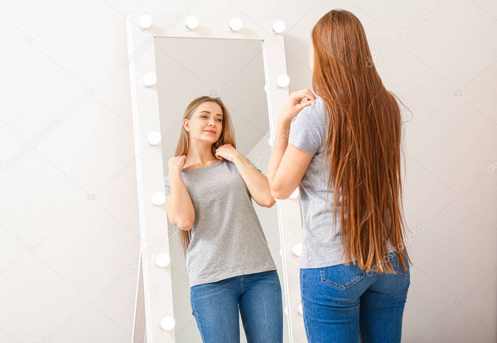 Beautiful young woman looking at her reflection in mirror