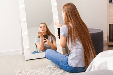 Güzel genç bir kadın evde aynanın önünde selfie çekiyor.