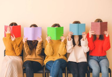 Kitapları olan genç kadınlar renk duvarının yanında oturuyor.