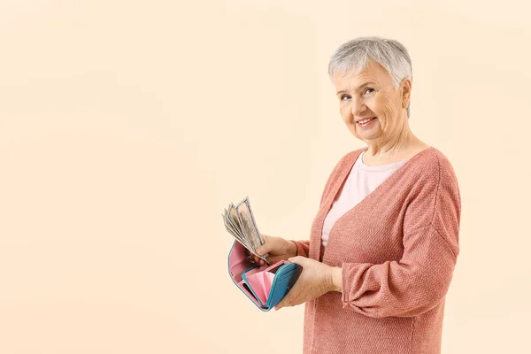 Senior woman with money on color background