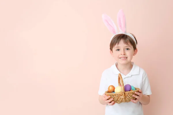 Little boy with Easter eggs and bunny ears on color background