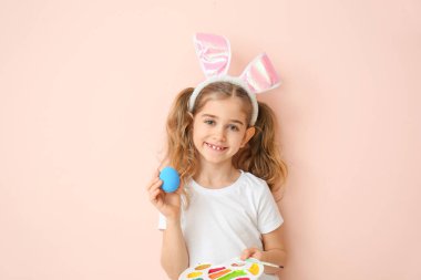 Paskalya yumurtası ve arka planda boya paleti olan küçük bir kız.