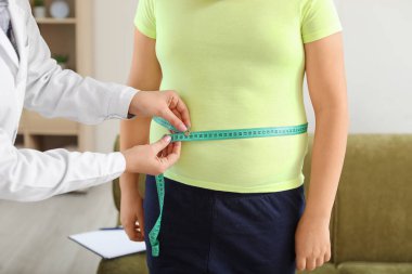 Doktor klinikte şişman çocuğu muayene ediyor.