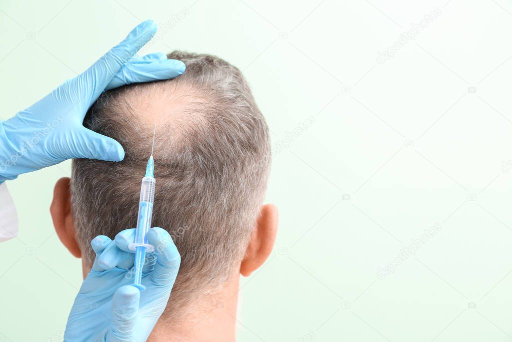 Senior man with hair loss problem receiving injection on color background