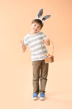 Paskalya yumurtası ve tavşan kulaklı küçük çocuk renk arka planında zafer jesti gösteriyor.