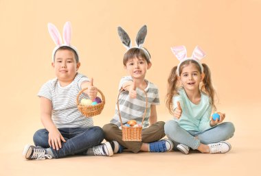 Paskalya yumurtası ve tavşan kulaklı küçük çocuklar renk arkaplanda baş parmak hareketi yapıyorlar.