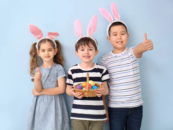 イースターエッグとウサギの耳を持つ小さな子供たちは 色の背景に親指アップジェスチャーを示しています — ストック写真