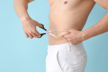 Makas tutan genç bir adam, arka planda göbeğine dokunuyor. Estetik ameliyat konsepti