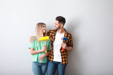 Yeni dairede ışıklı duvarın yanında boya rulosu olan genç bir çift.