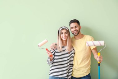 Yeni dairede renkli duvarların yanında boya ruloları olan genç bir çift.