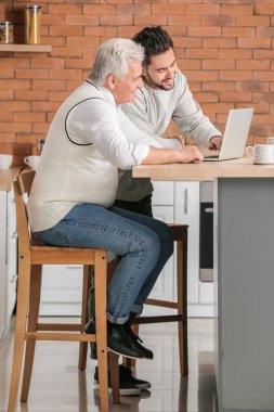 Genç adam ve babası mutfakta dizüstü bilgisayarları var.