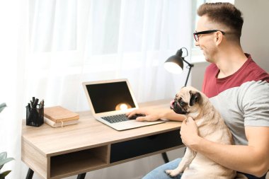 Evde sevimli köpekli ve dizüstü bilgisayarı olan yakışıklı bir adam.