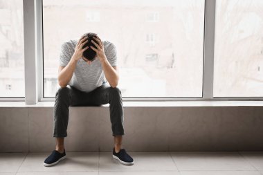 Depresyondaki genç adam pencerenin yanında