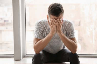 Depresyondaki genç adam pencerenin yanında