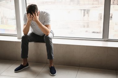 Depresyondaki genç adam pencerenin yanında