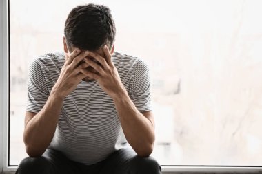 Depresyondaki genç adam pencerenin yanında