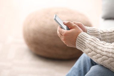 Young man with mobile phone at home, closeup