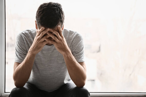 Depressed young man near window