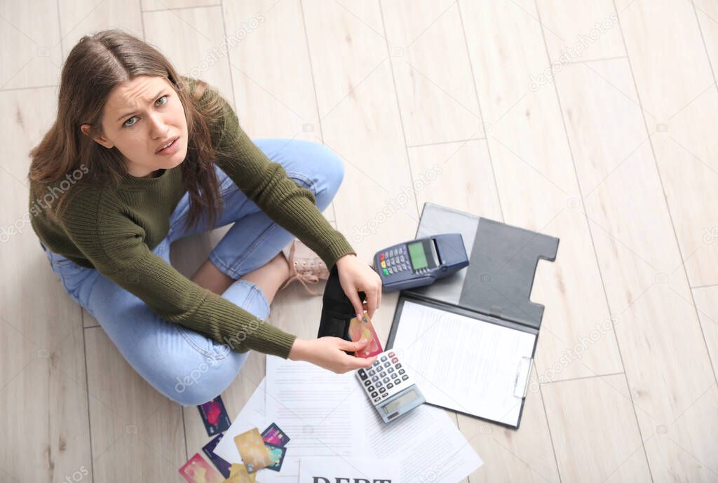 Worried young woman in debt at home, top view