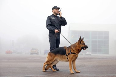 Sokak ortasında devriye gezen köpekli bir erkek polis memuru.
