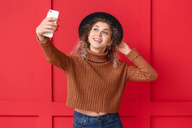 Kalın kazaklı güzel bir kadın arka planda selfie çekiyor.