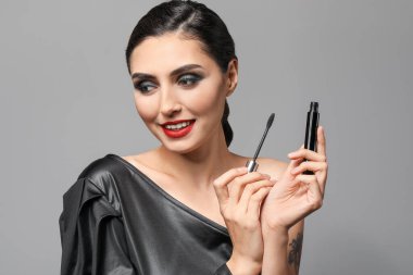 Gri arka plana makyaj yapan güzel bir genç kadın.