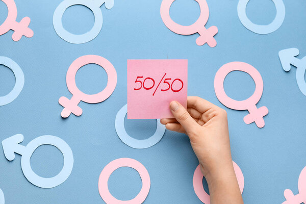Женская рука с бумажным листом и символами женщины и мужчины на цветном фоне. Понятие феминизма
