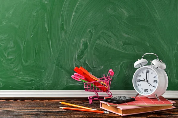 Set of school supplies, shopping cart and clock on table