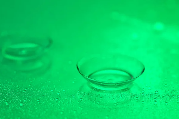 Contact lens and water drops on color background